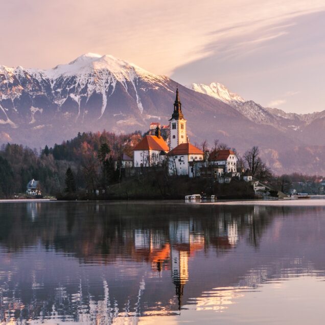 brown and white concrete building near lake and mountain under white clouds during daytime